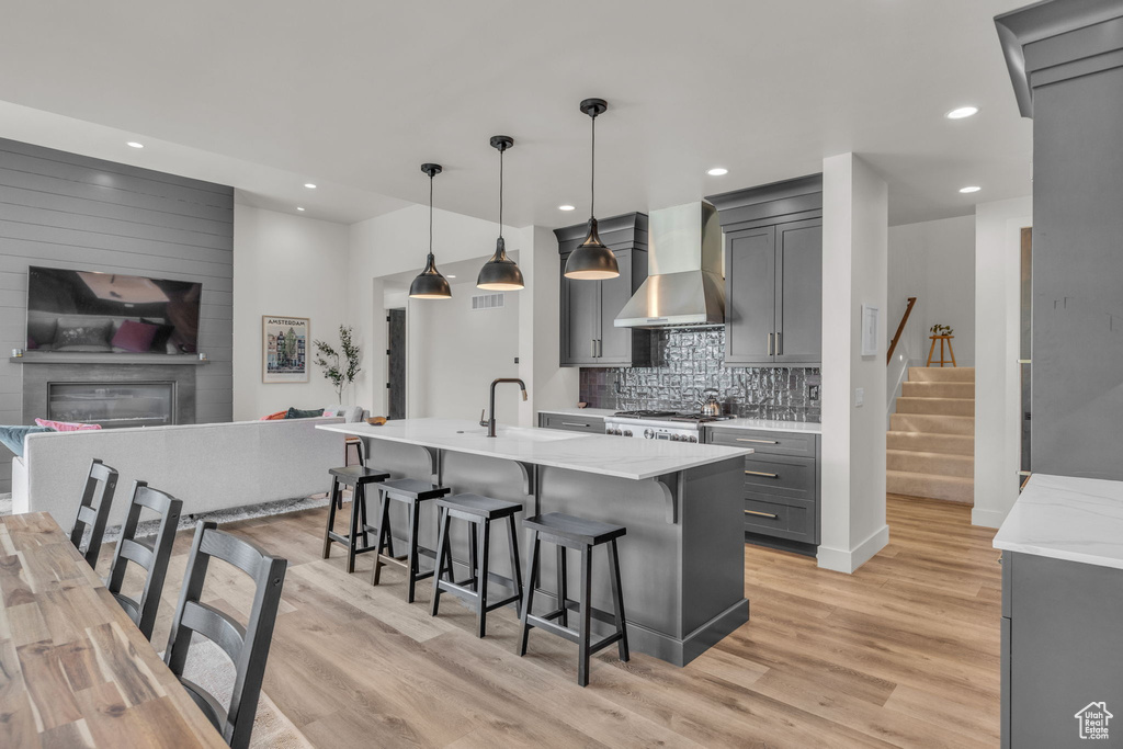 Kitchen featuring wall chimney range hood, gray cabinets, range, a sink, and light wood-type flooring