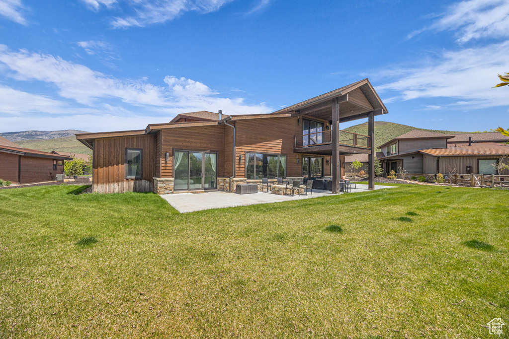 Rear view of property featuring a balcony, a patio area, a yard, and stone siding