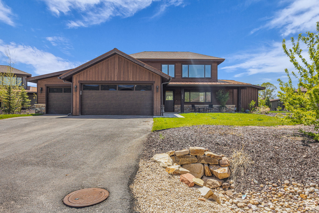 View of front of home with stone siding, driveway, a front yard, and an attached garage