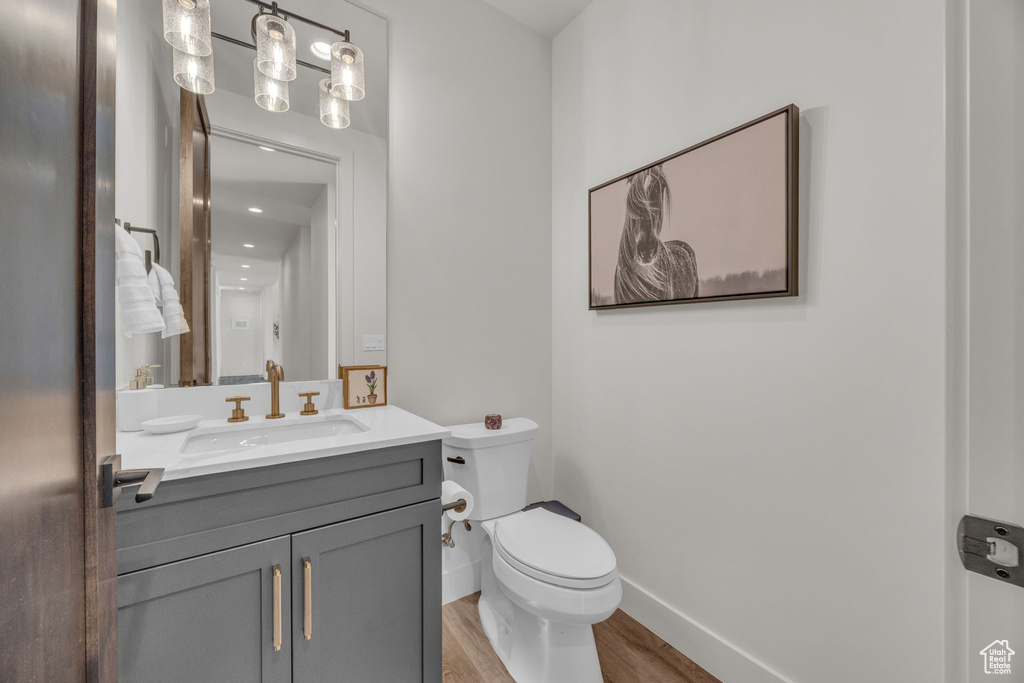 Half bath with toilet, vanity, baseboards, and wood finished floors