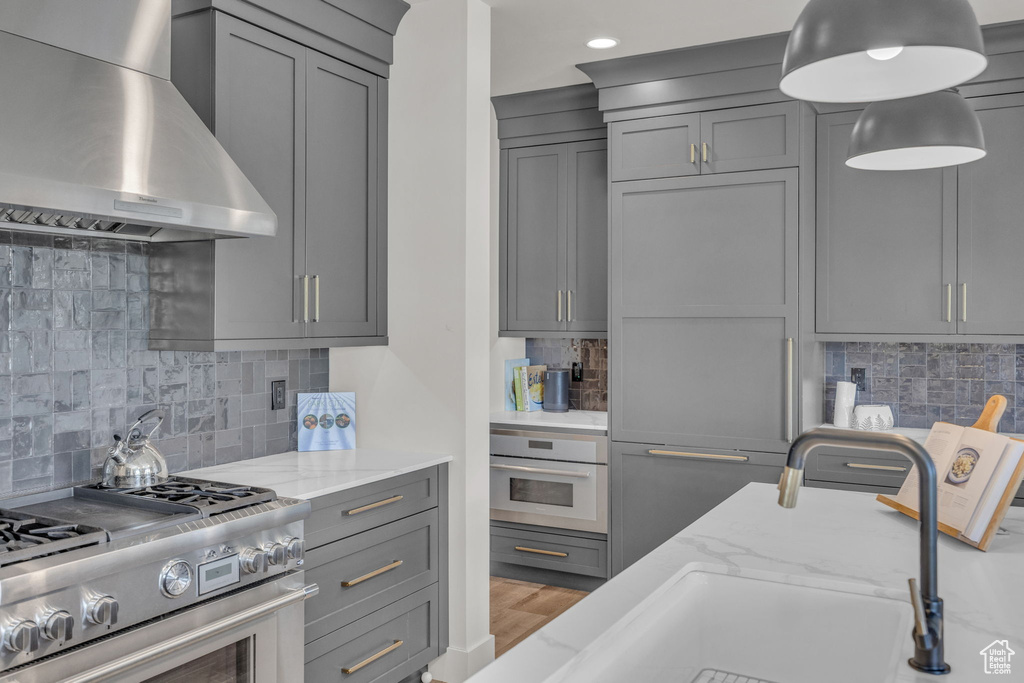 Kitchen featuring wall chimney range hood, stainless steel appliances, gray cabinets, backsplash, and recessed lighting