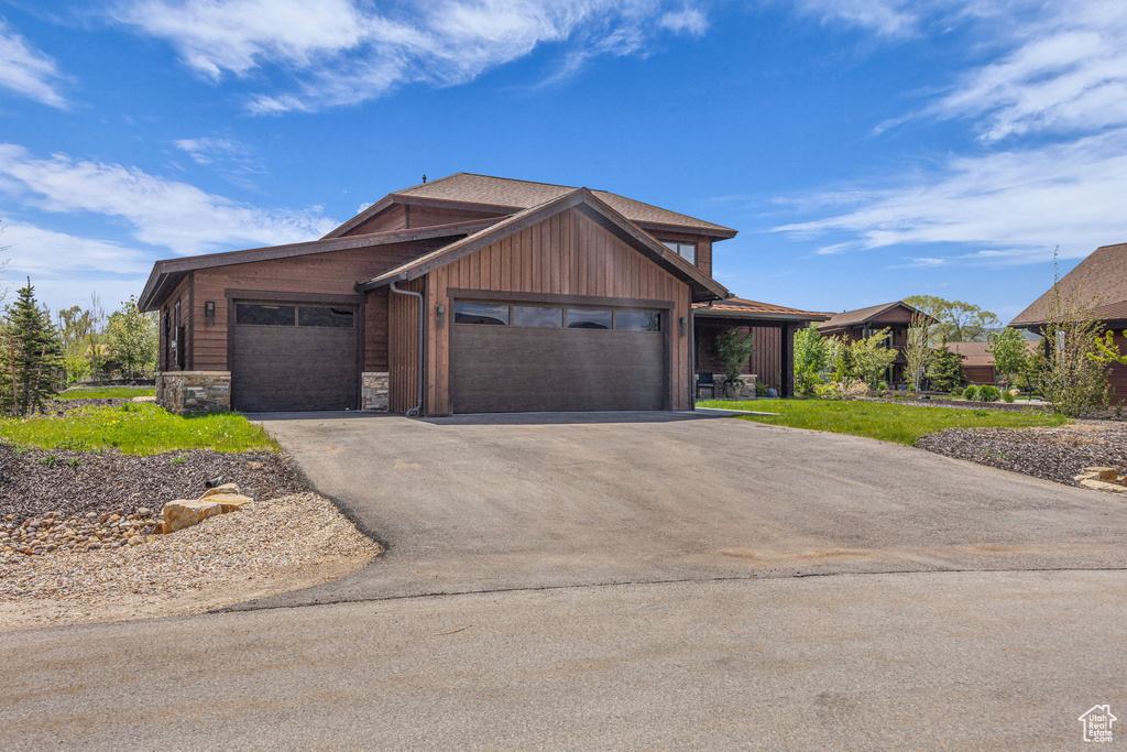 View of front facade featuring asphalt driveway, an attached garage, and stone siding