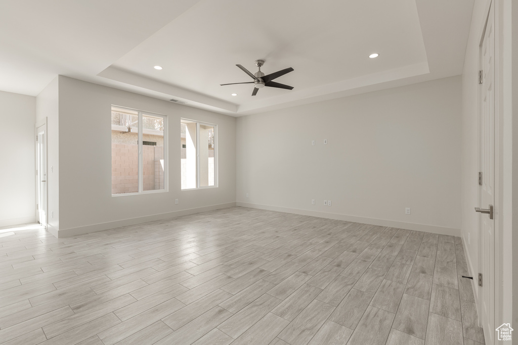 Unfurnished room featuring a tray ceiling, a ceiling fan, light wood-style floors, recessed lighting, and baseboards