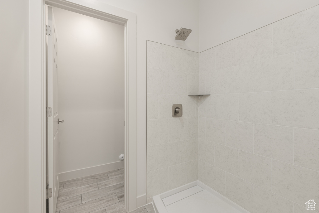 Full bathroom with a tile shower, baseboards, and wood finished floors