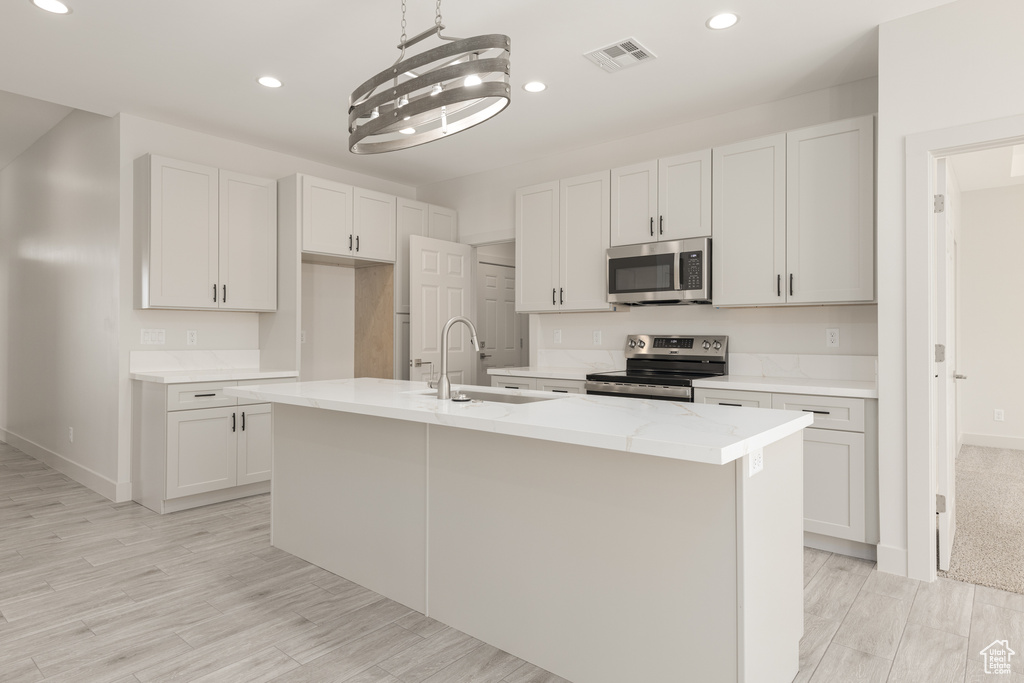 Kitchen featuring stainless steel appliances, recessed lighting, a center island with sink, baseboards, and light wood-style flooring