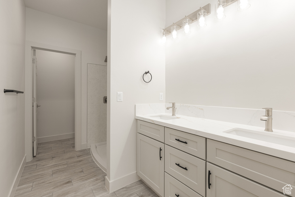 Full bathroom featuring a walk in shower, double vanity, baseboards, and wood finished floors
