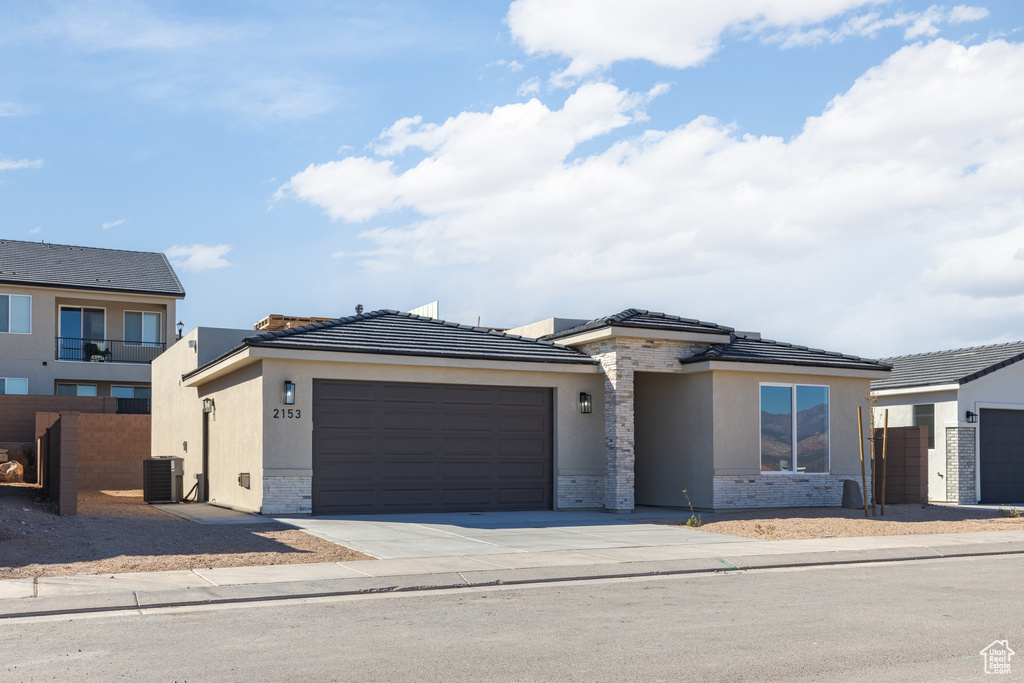 View of front of house featuring an attached garage, cooling unit, stone siding, driveway, and stucco siding