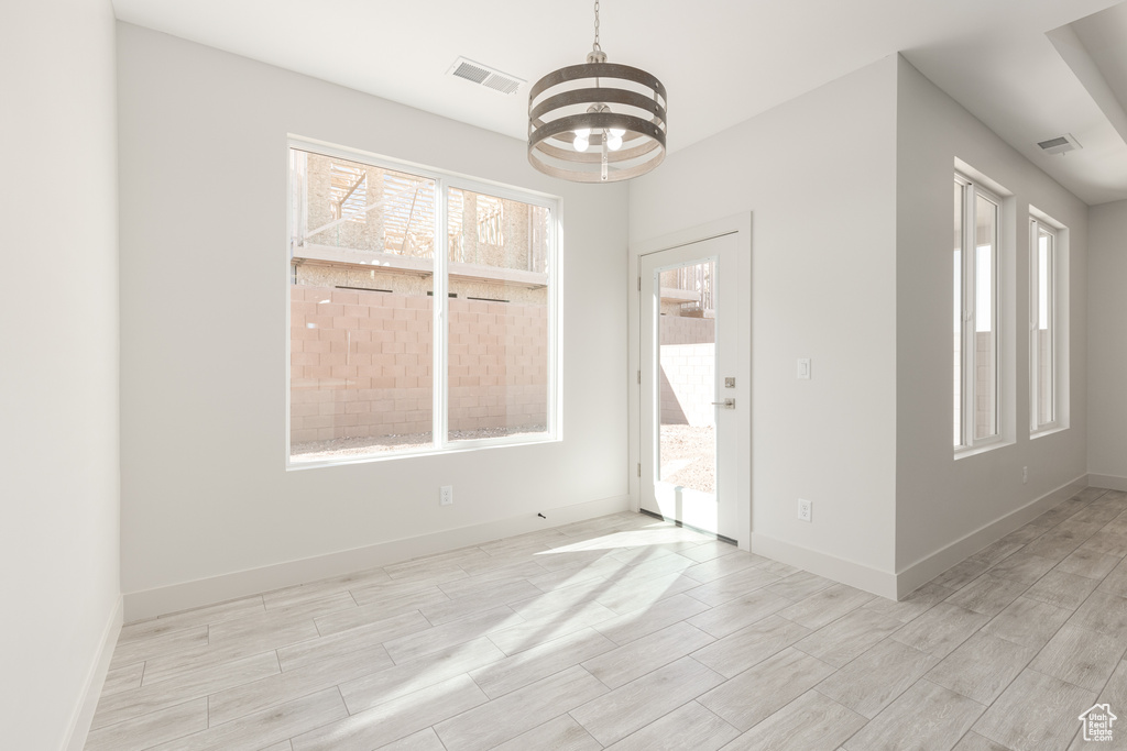 Unfurnished room featuring healthy amount of natural light, a chandelier, and wood tiled floors