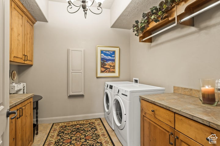 Laundry area with washing machine and dryer, cabinet space, baseboards, light tile patterned floors, and a chandelier