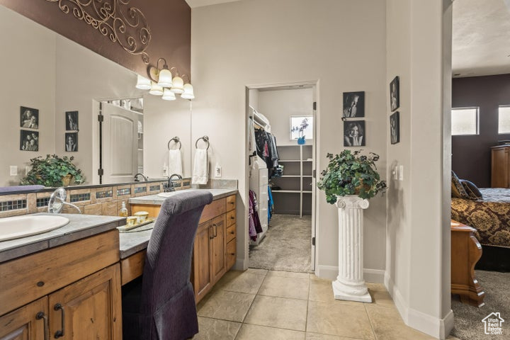 Ensuite bathroom with double vanity, tile patterned floors, a walk in closet, and baseboards