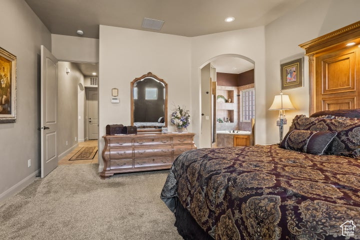 Carpeted bedroom featuring arched walkways, ensuite bath, and recessed lighting