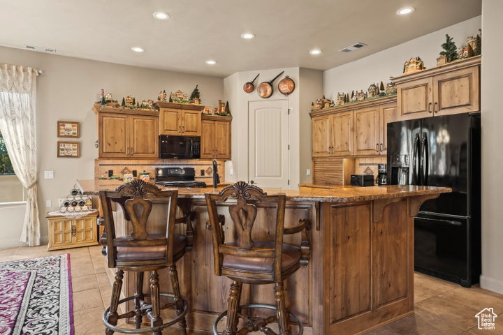 Kitchen with black appliances, light stone counters, recessed lighting, light tile patterned floors, and backsplash