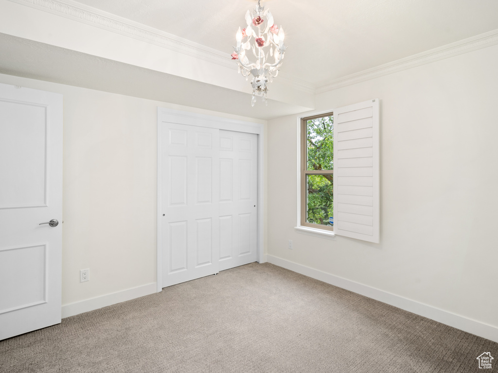 Unfurnished bedroom featuring a chandelier, ornamental molding, baseboards, carpet, and a closet