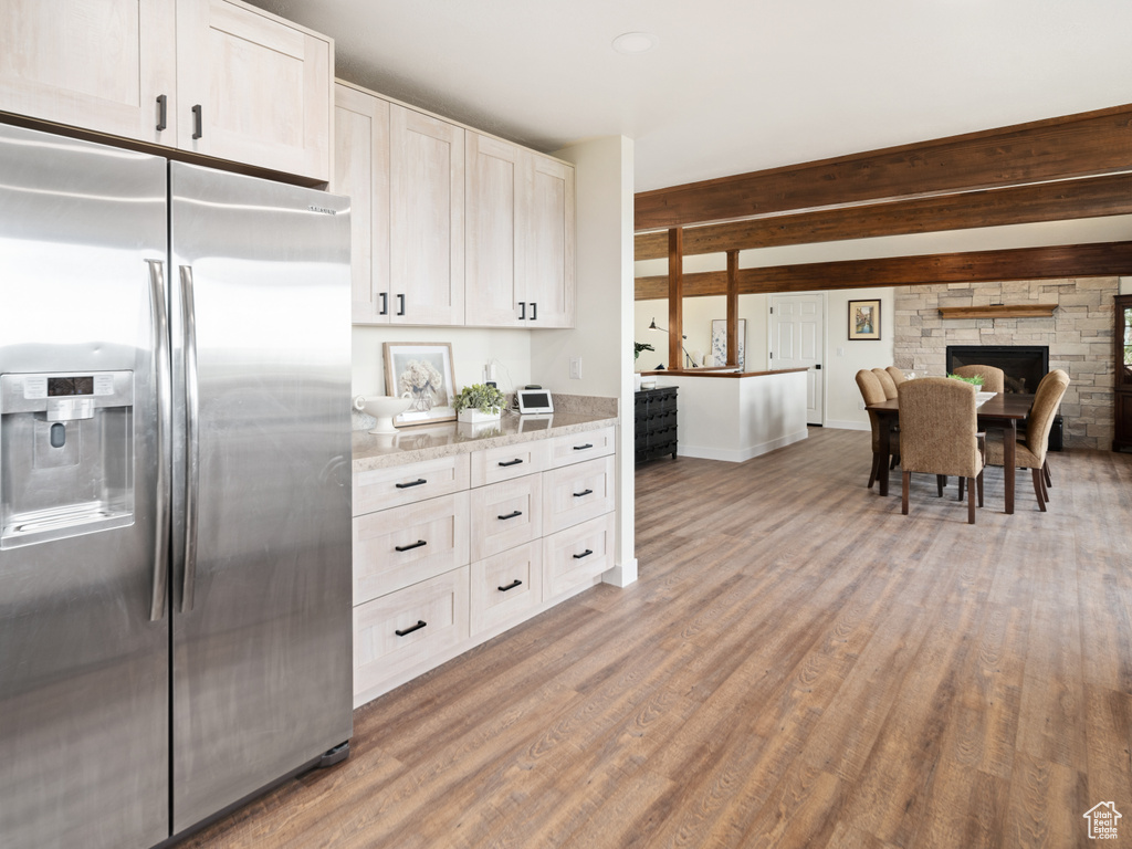 Kitchen featuring stainless steel refrigerator with ice dispenser, light wood-style flooring, light stone counters, baseboards, and white cabinets