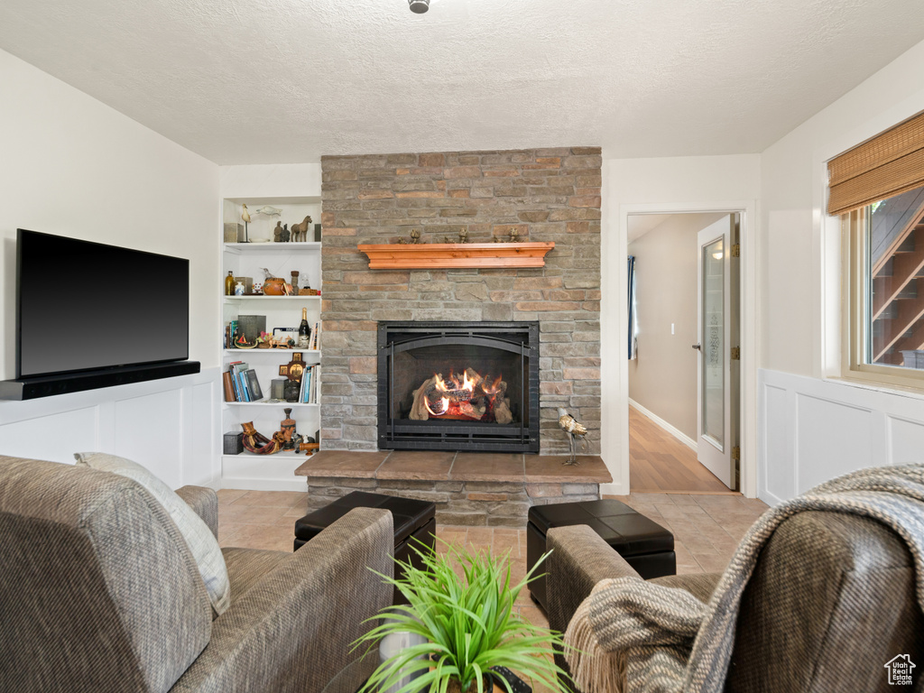 Living room with a fireplace, built in features, a textured ceiling, and a wainscoted wall