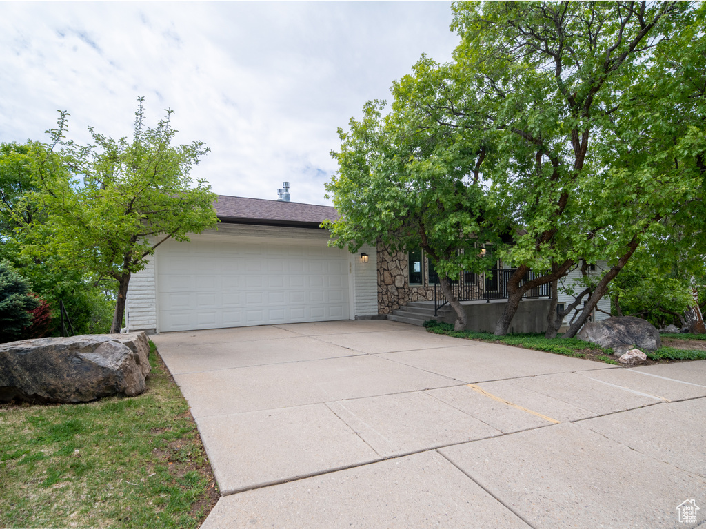 View of property hidden behind natural elements featuring driveway, a garage, and stone siding