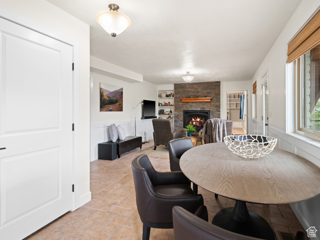 Dining space with built in features, a stone fireplace, and light stone finish flooring
