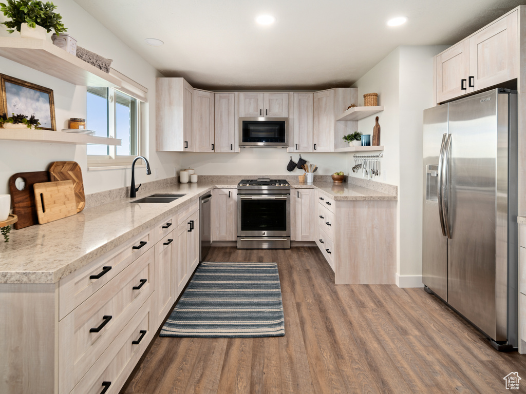 Kitchen featuring appliances with stainless steel finishes, a sink, open shelves, dark wood-style flooring, and light stone counters