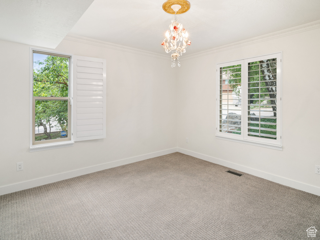 Empty room featuring healthy amount of natural light, baseboards, a chandelier, crown molding, and carpet flooring