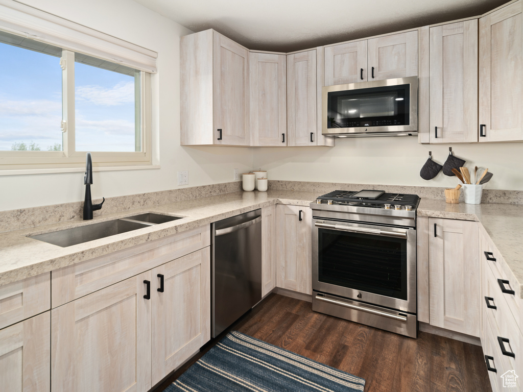 Kitchen with appliances with stainless steel finishes, a sink, dark wood-style floors, and light stone countertops