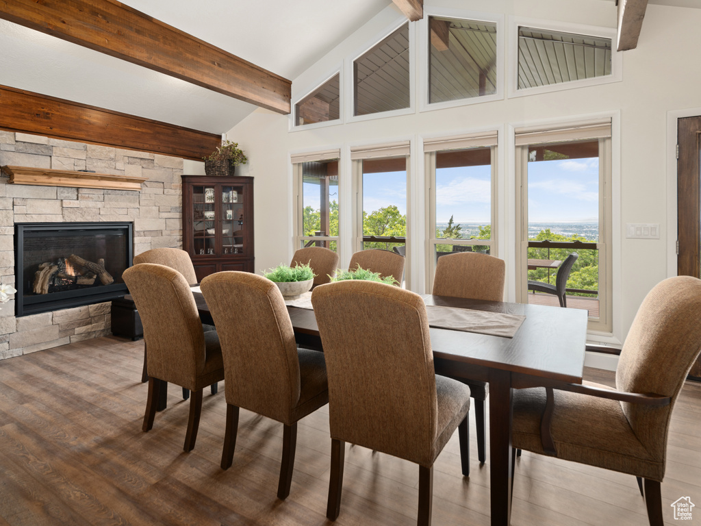 Dining room with wood finished floors, beam ceiling, a stone fireplace, and high vaulted ceiling