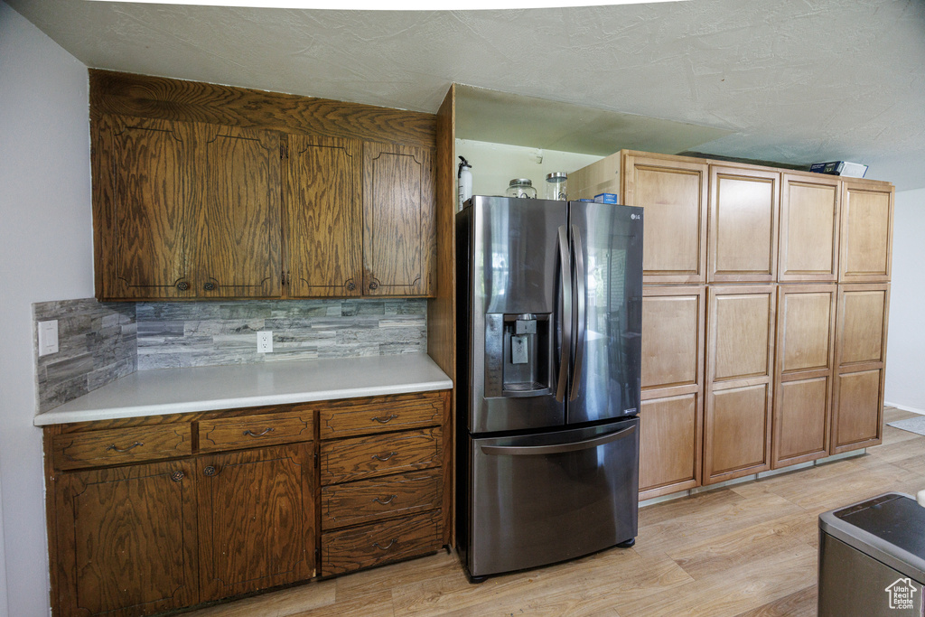 Kitchen featuring stainless steel fridge, light wood-style floors, backsplash, and light countertops