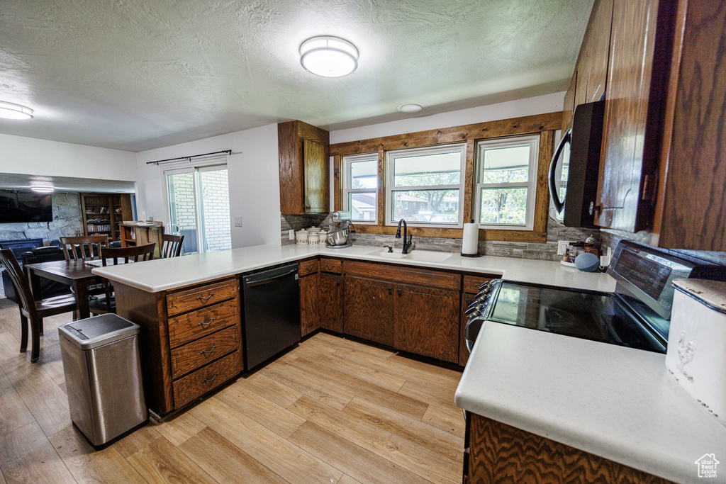 Kitchen with black appliances, a sink, light wood finished floors, a peninsula, and a textured ceiling