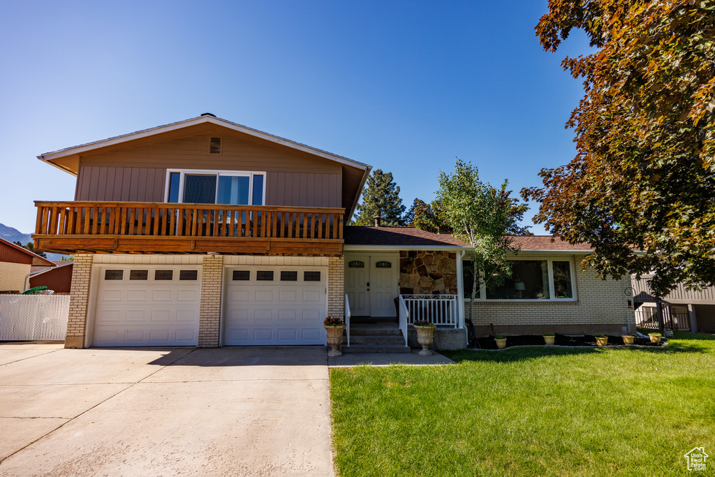 Tri-level home with concrete driveway, a front lawn, a garage, brick siding, and a porch