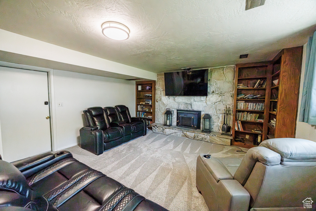 Living room featuring carpet flooring, a stone fireplace, a textured ceiling, and baseboards
