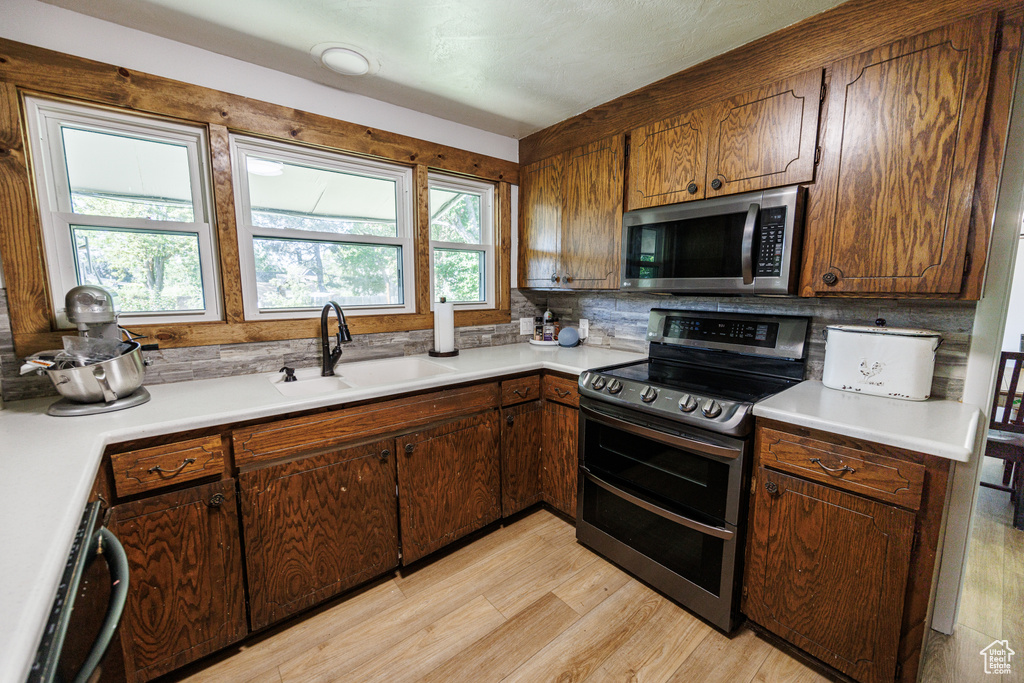 Kitchen with appliances with stainless steel finishes, a sink, light wood-type flooring, and light countertops