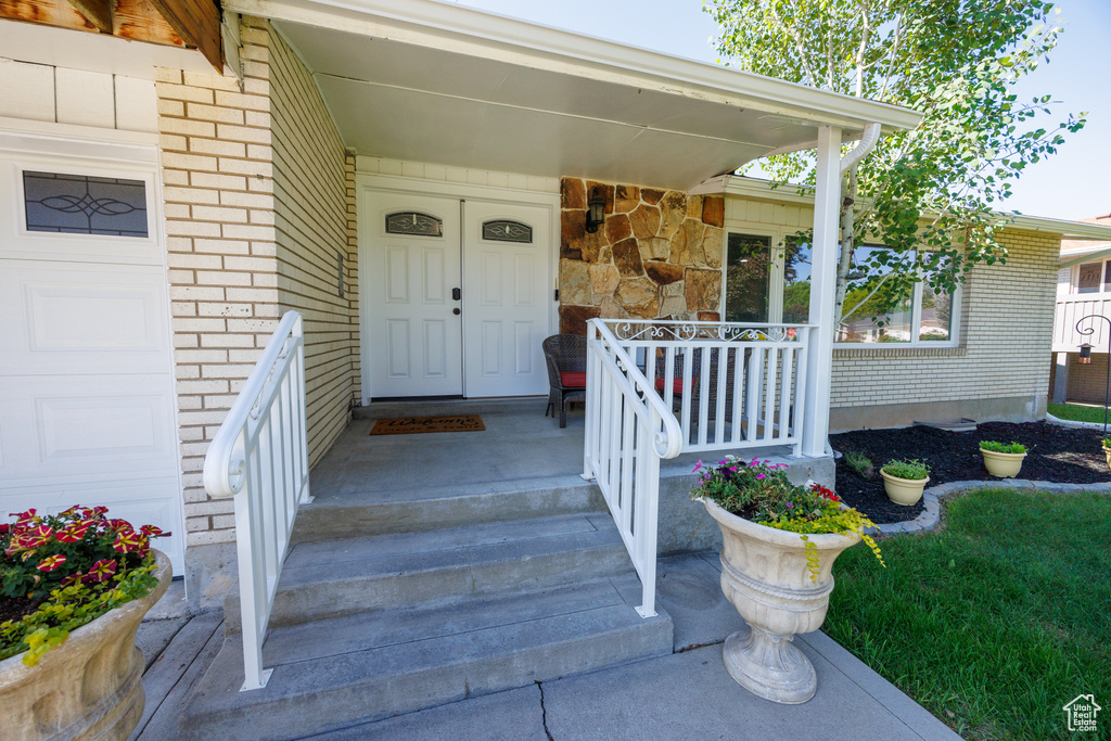 View of exterior entry featuring a porch, brick siding, and a garage