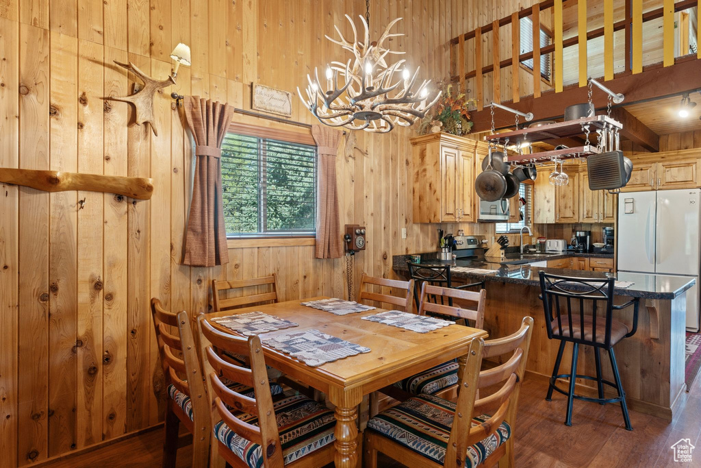 Dining room featuring wood walls, a chandelier, dark wood finished floors, and a high ceiling