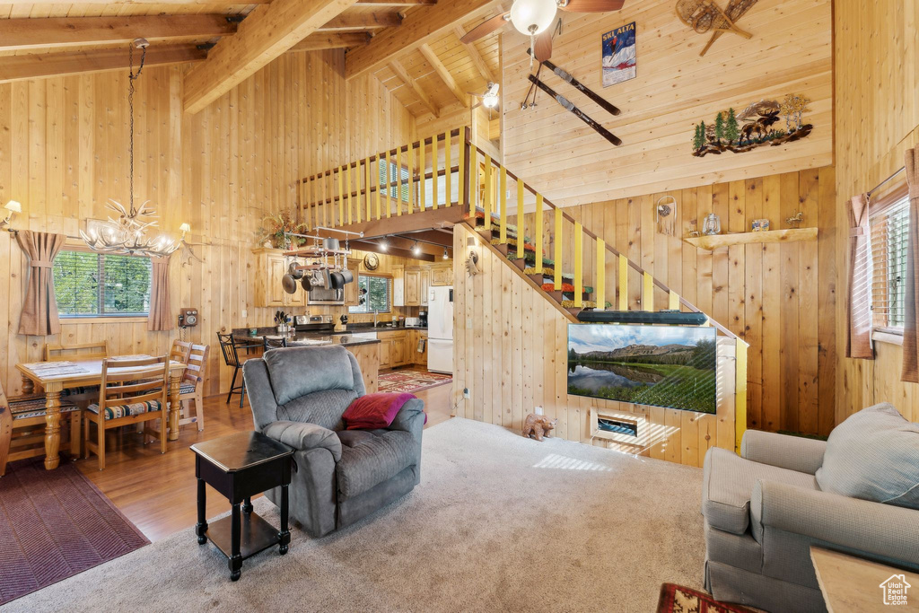 Living area featuring high vaulted ceiling, wood walls, a chandelier, stairway, and a ceiling fan