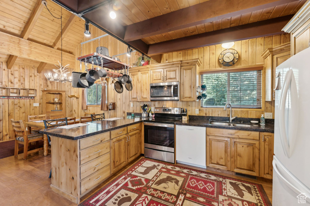 Kitchen with stainless steel appliances, a sink, wooden walls, wooden ceiling with exposed beams, and a peninsula