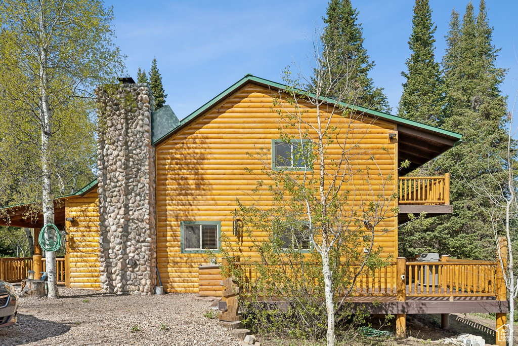 View of home's exterior featuring a chimney, a deck, a balcony, and faux log siding