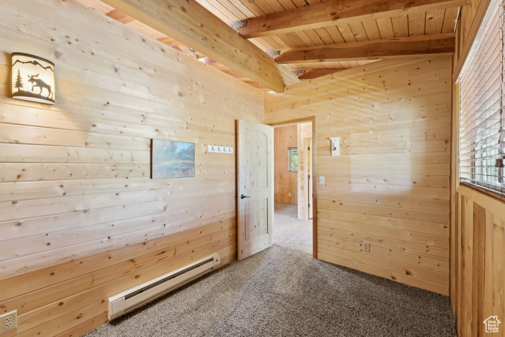 Carpeted empty room with baseboard heating, wooden ceiling with exposed beams, and wooden walls