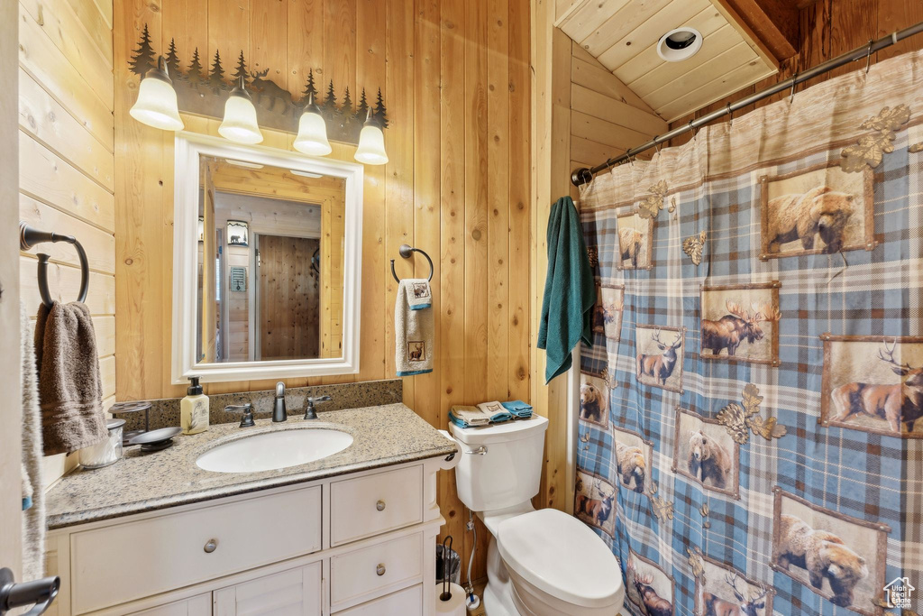 Bathroom featuring wooden walls, toilet, vanity, lofted ceiling, and a shower with shower curtain