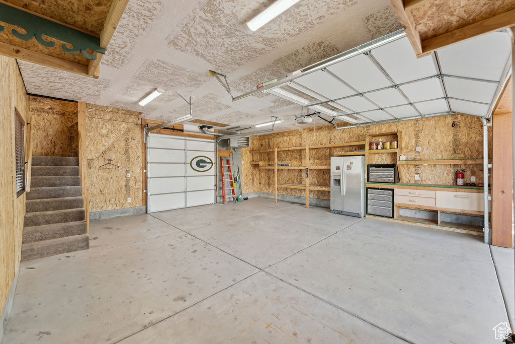 Garage with white refrigerator with ice dispenser, a garage door opener, and a workshop area