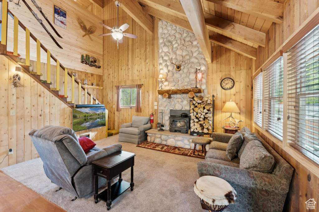 Living room featuring a wood stove, wood walls, wood ceiling with exposed beams, high vaulted ceiling, and ceiling fan
