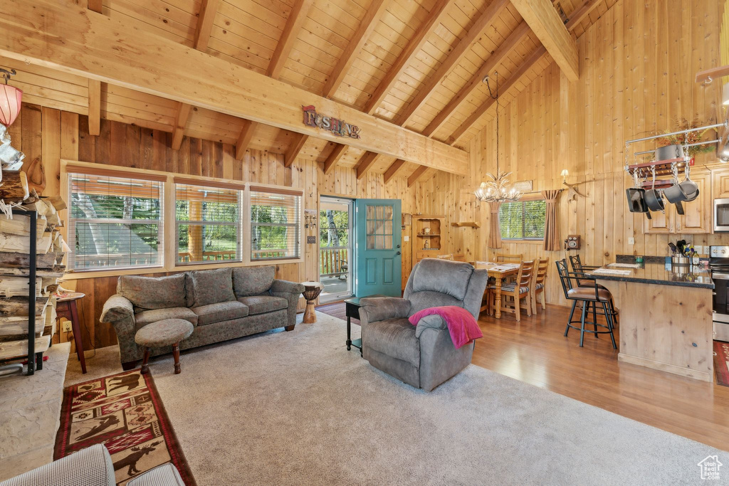 Carpeted living area featuring wooden walls, a chandelier, wooden ceiling with exposed beams, high vaulted ceiling, and wood finished floors