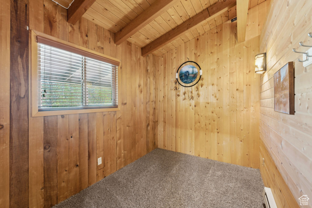 Carpeted empty room featuring wood walls, wooden ceiling with exposed beams, and a baseboard radiator