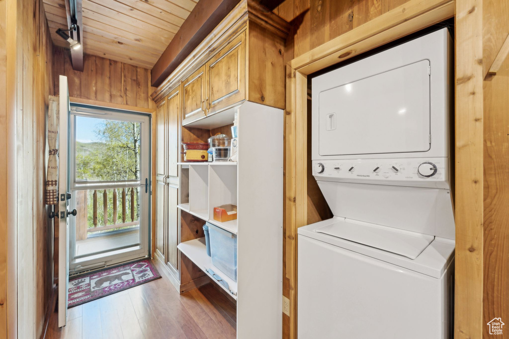 Laundry room with stacked washer and clothes dryer, wooden ceiling, wood finished floors, and wooden walls