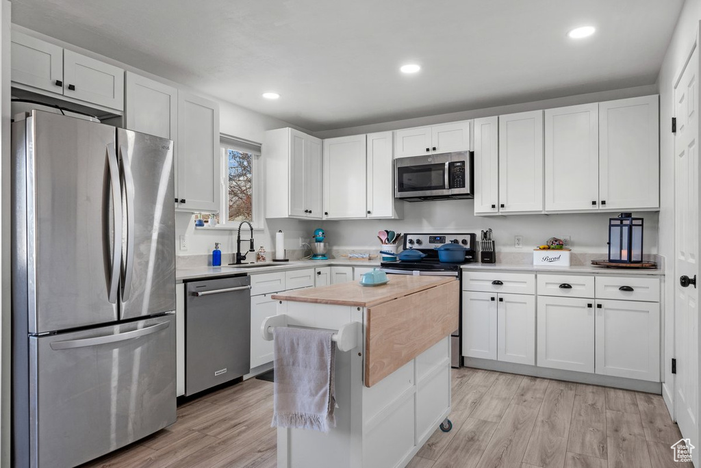 Kitchen with stainless steel appliances, a sink, white cabinets, light wood-style flooring, and recessed lighting