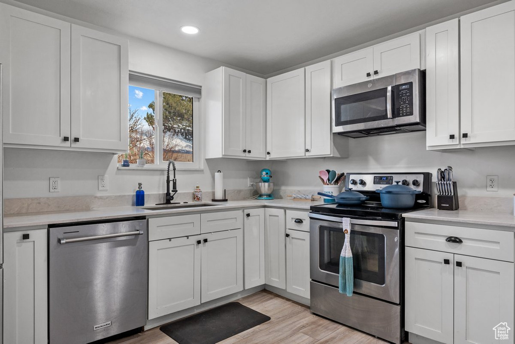 Kitchen featuring appliances with stainless steel finishes, a sink, white cabinetry, light countertops, and recessed lighting