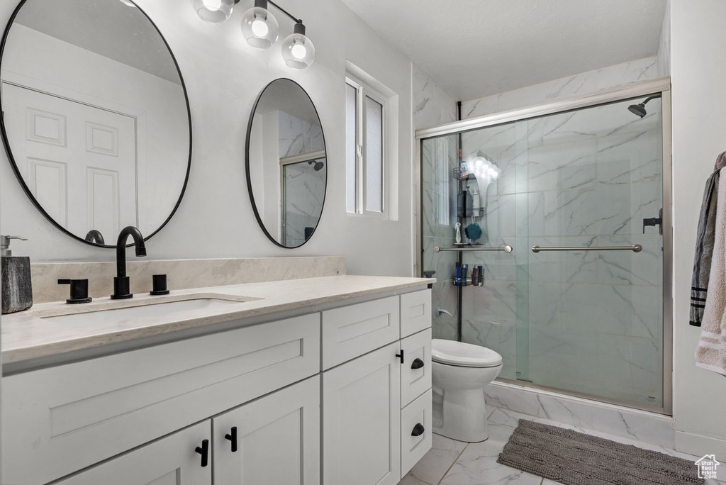 Bathroom with marble look tile flooring, vanity, toilet, and a marble finish shower