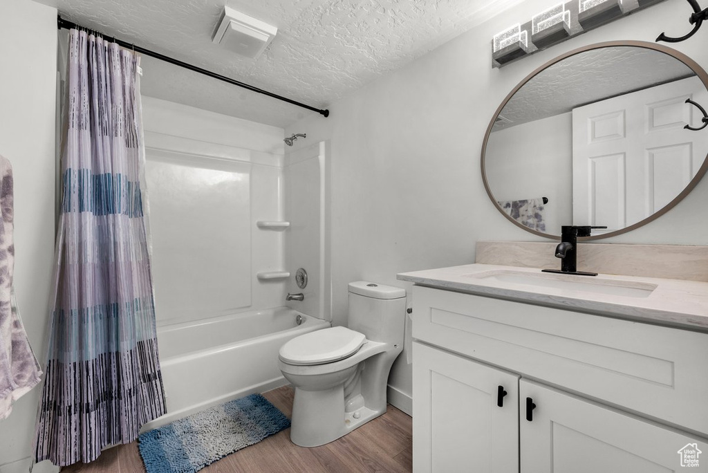 Full bathroom featuring wood finished floors, shower / tub combo, a textured ceiling, vanity, and toilet