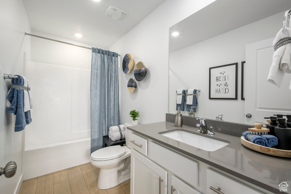 Bathroom with vanity, recessed lighting, toilet, shower / tub combo, and wood finished floors