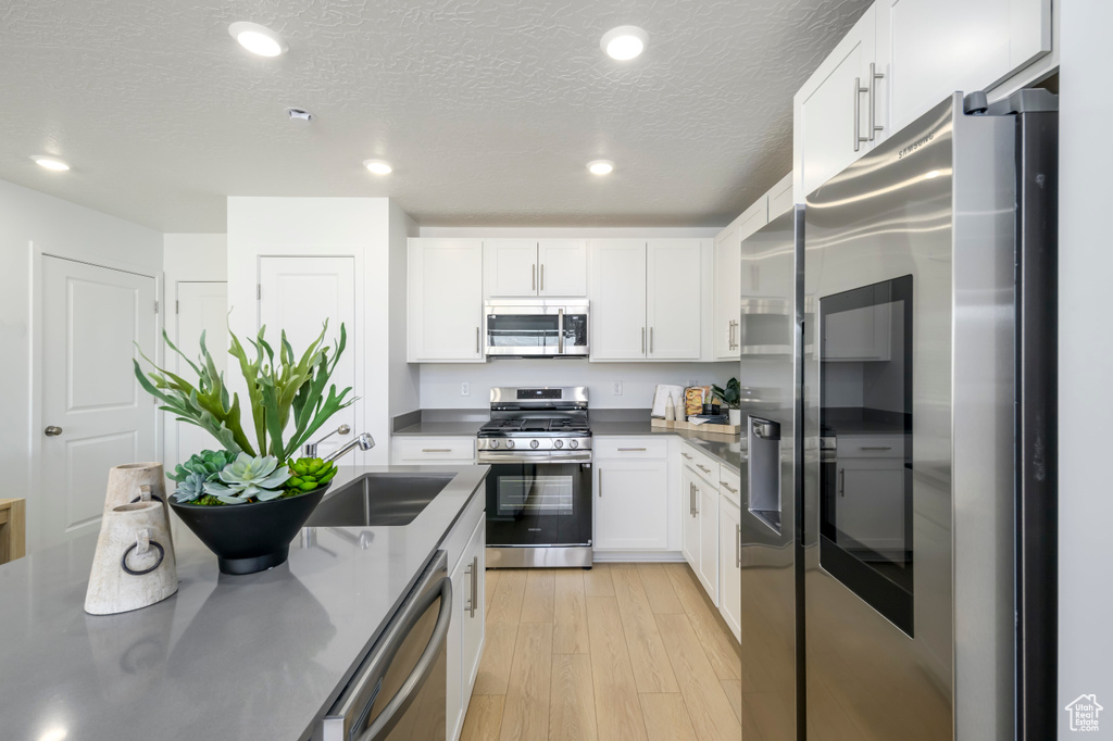 Kitchen featuring appliances with stainless steel finishes, a sink, white cabinets, light wood-style floors, and a textured ceiling
