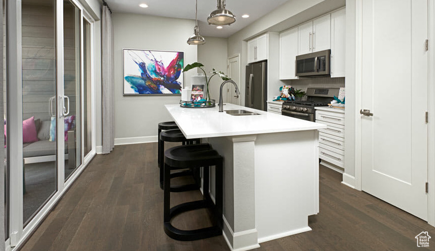 Kitchen with stainless steel appliances, a sink, an island with sink, recessed lighting, and baseboards