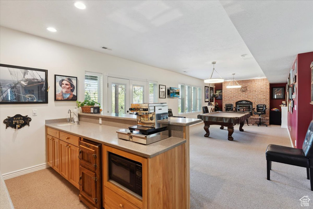 Kitchen with a peninsula, a sink, black microwave, light carpet, and pool table